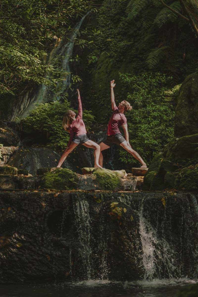 Couple Practicing Yoga By Tropical Waterfall