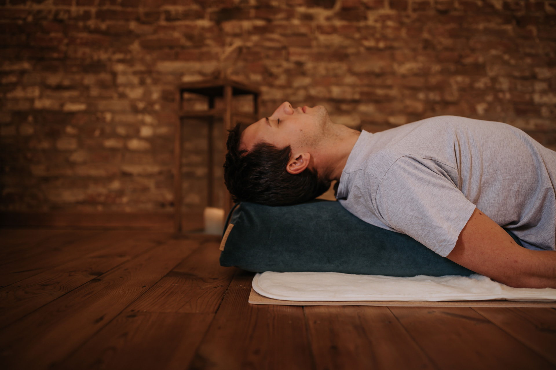 Personne allongée en arrière sur un bolster PIERRE bleu canard sur un parquet